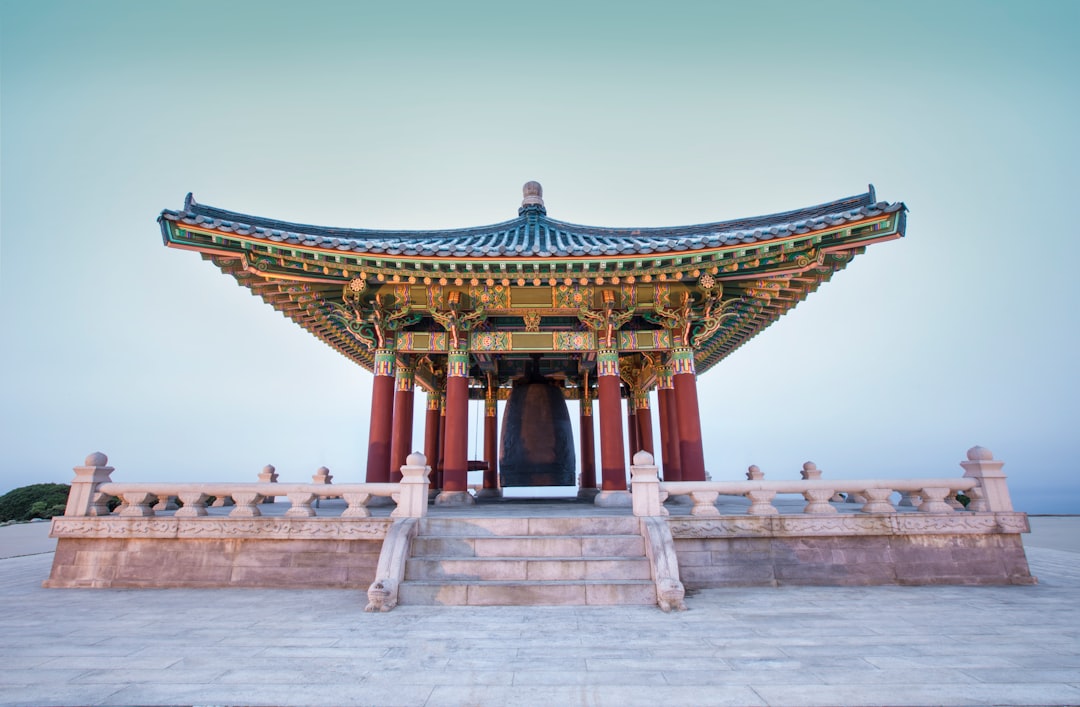 한국 F-5 영주비자를 나타내는 영주증 카드를 들고 있는 손. 도시 배경은 한국에서의 안정적인 삶을 상징합니다.
